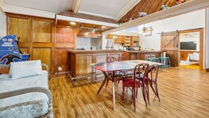 A spacious living area with a wooden floor, a dining table with chairs, a kitchen with wooden cabinets, and a large window. - Enormous Historic Treme Pad by French Quarter (New Orleans)