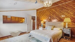 A bedroom with a wooden hipped roof ceiling, a bed with a striped bedspread, two bedside lamps, and a nightstand with a lamp. - Enormous Historic Treme Pad by French Quarter (New Orleans)