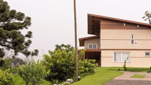 Una casa moderna de dos pisos con techo inclinado, terraza de madera y jardín cuidado con diversas plantas y flores.