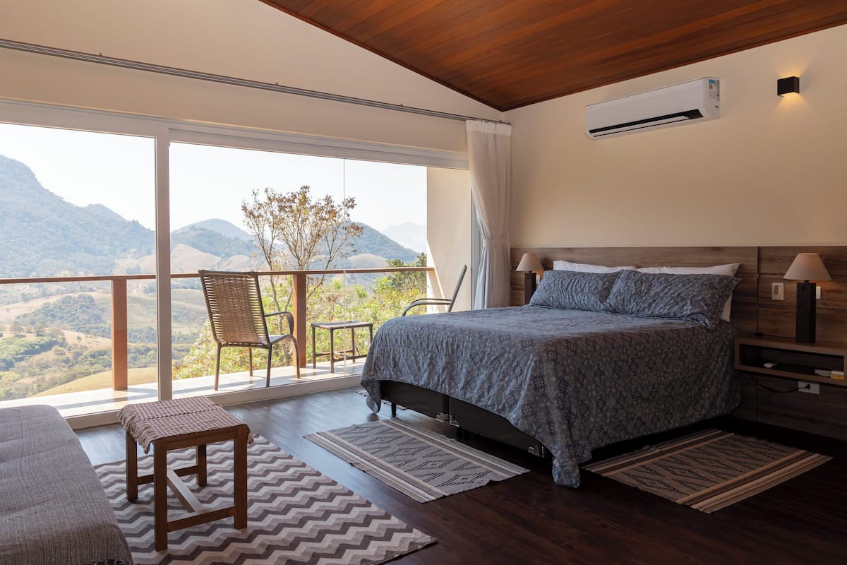 A bedroom with a large window, a bed, a chair, and a nightstand.
