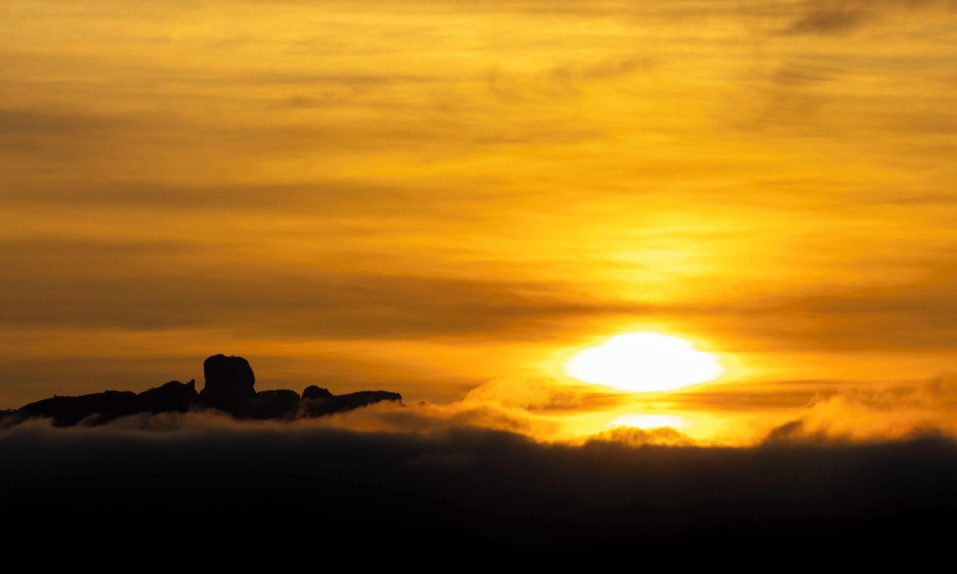A sunset over a mountainous landscape with clouds below.