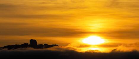 A sunset over a mountainous landscape with clouds below.