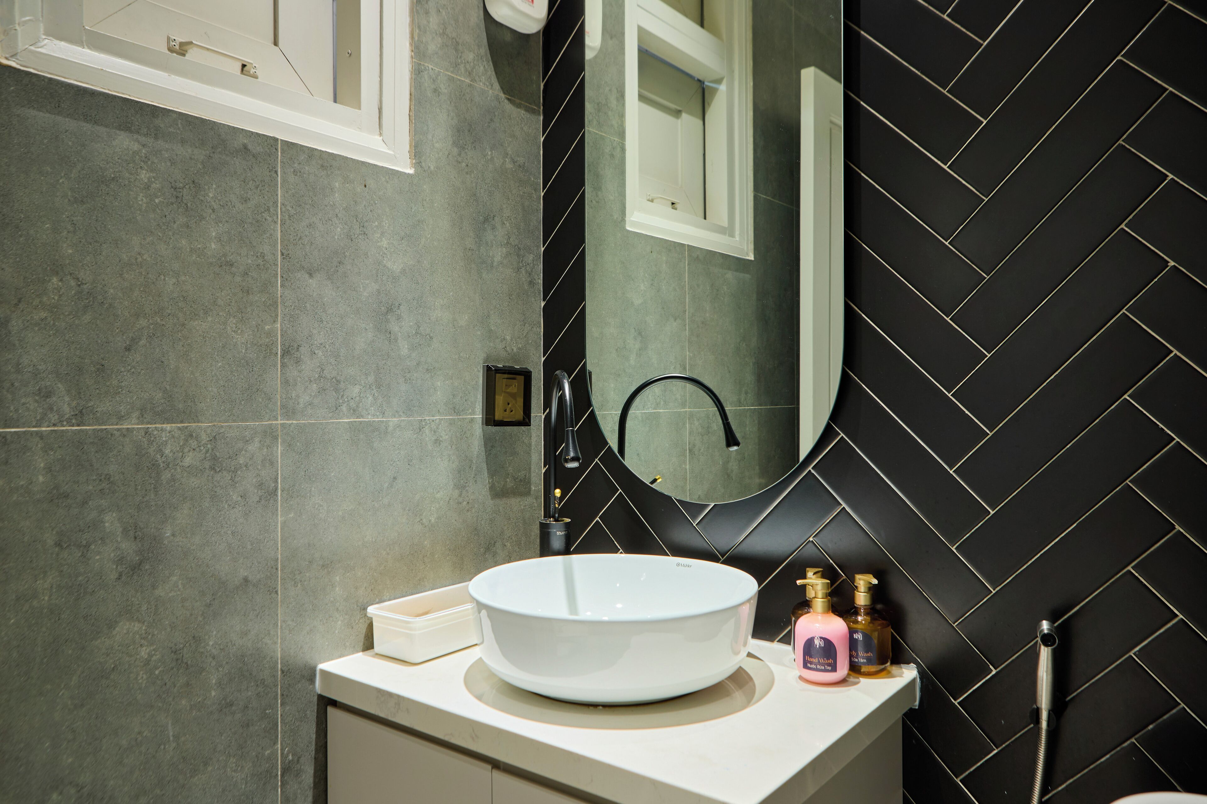 A bathroom with a white sink, a mirror, and a black tiled wall.
