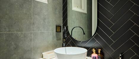 A bathroom with a white sink, a mirror, and a black tiled wall.