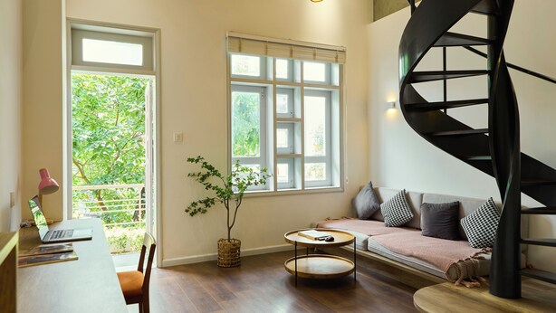 A modern living room with a spiral staircase, a wooden desk with a laptop, a round table, and a sofa with cushions. - Kin Wander Tan Quy (Ho Chi Minh City)