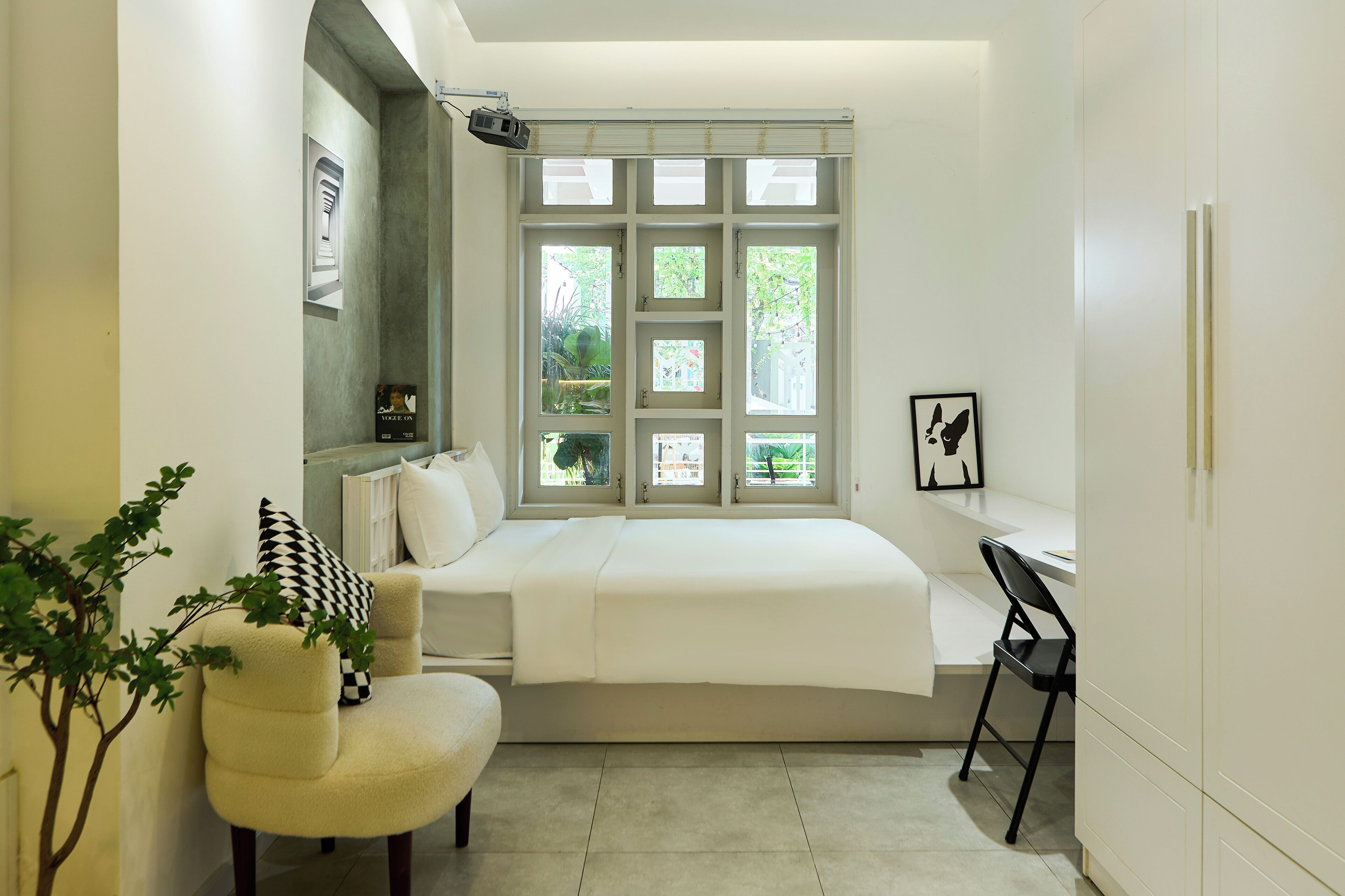 A bedroom with a bed, a desk, a chair, a window with multiple panes, and a plant.