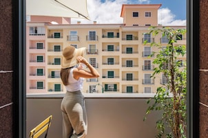 Un balcon donnant sur des immeubles à étages, une plante en pot et une chaise jaune.