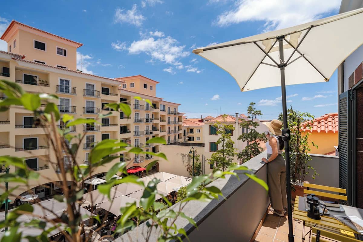 Un balcon avec une table et des chaises, un grand parasol et une vue sur un immeuble à plusieurs étages doté de balcons.