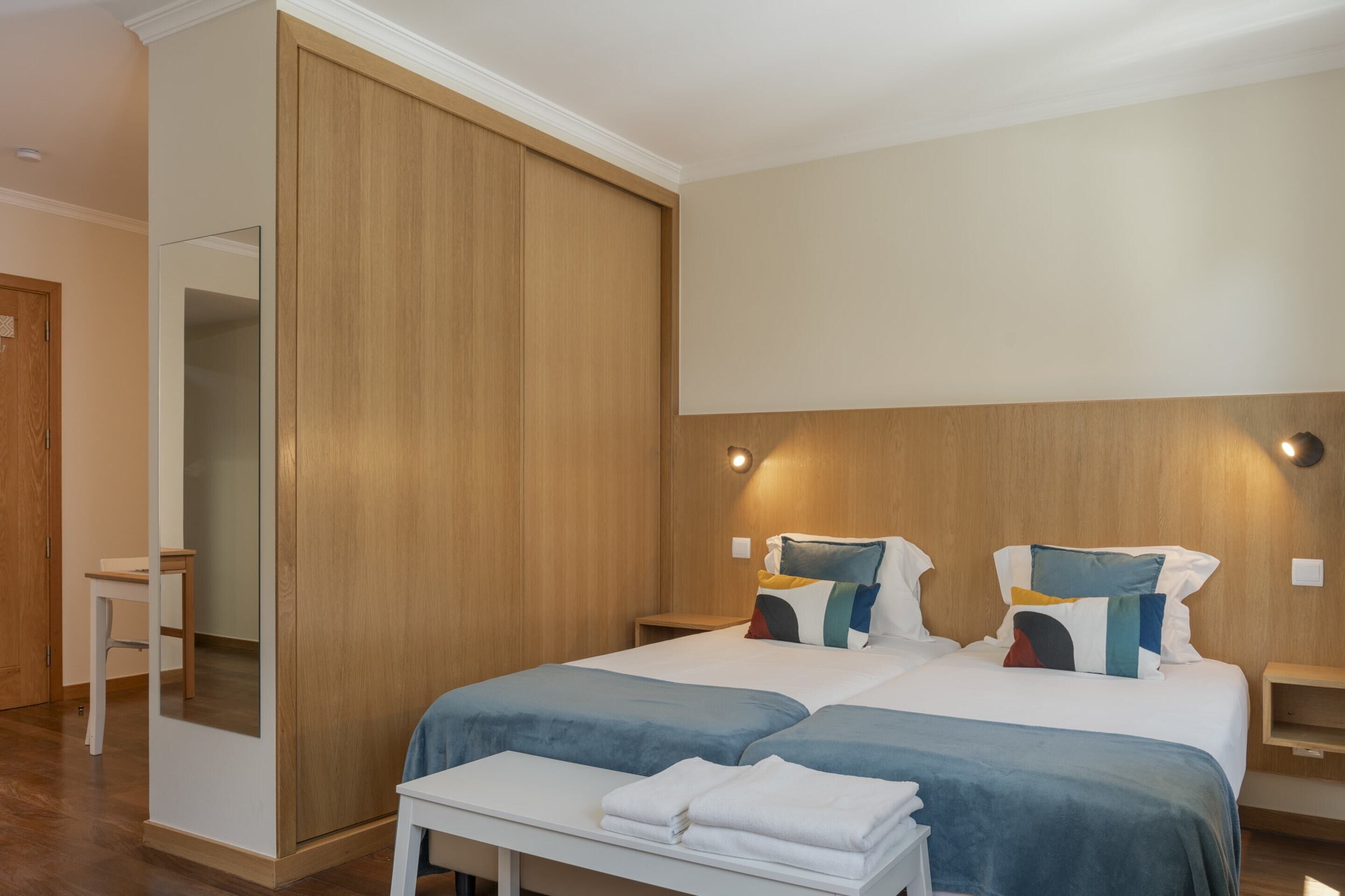 Una moderna camera d'hotel con un letto grande, due comodini, un armadio in legno e uno specchio.