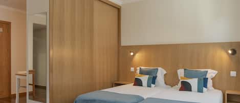 A modern hotel room with a large bed, two bedside tables, a wooden wardrobe, and a mirror.