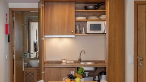 Une cuisine compacte avec des meubles en bois, un four à micro-ondes, un évier et un panier de fruits sur la table.