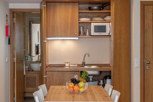Une cuisine compacte avec des meubles en bois, un four à micro-ondes, un évier et un panier de fruits sur la table.