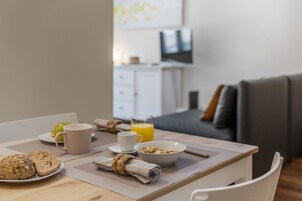 Une table de petit-déjeuner avec une assiette de toasts, un bol de céréales, une tasse et un verre de jus d’orange.