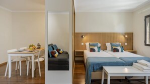 Une chambre d’hôtel moderne comprenant un coin repas, un canapé, deux lits et une petite table.