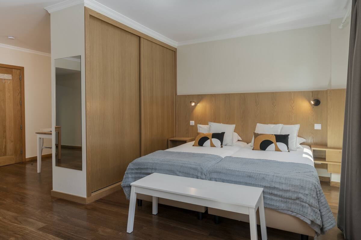 Une chambre moderne avec un grand lit, une armoire en bois, des tables de chevet et un banc.