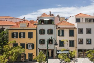 A row of colorful buildings with red-tiled roofs and green shutters, featuring a central building with a balcony.