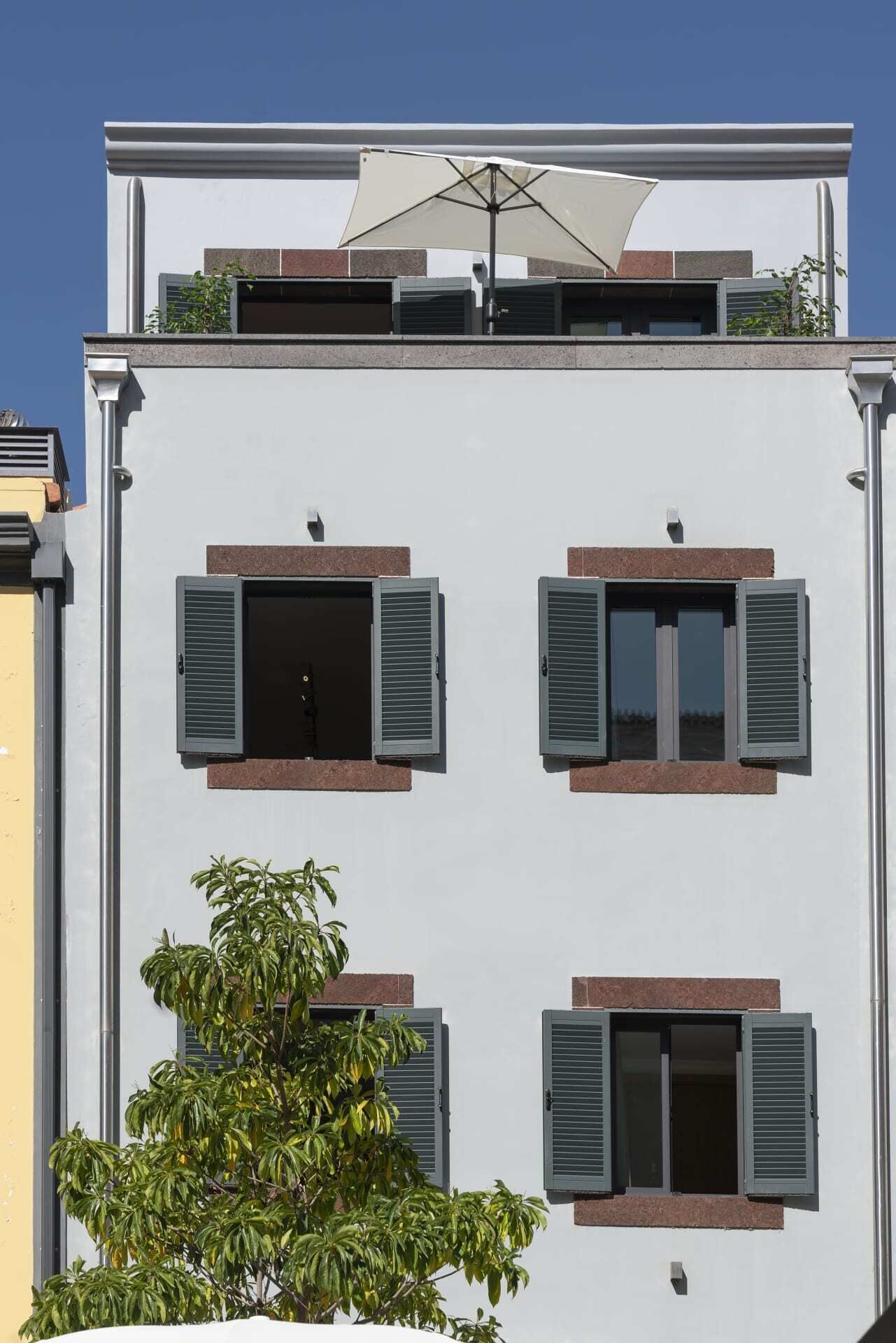 A modern building with four windows, each with shutters, and a balcony with a white awning.