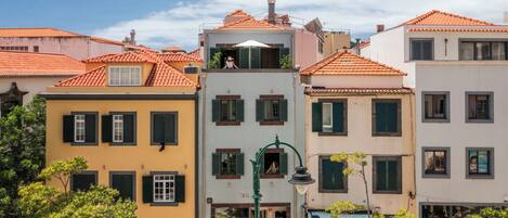 A row of colorful buildings with red-tiled roofs and green shutters, featuring a central building with a balcony.