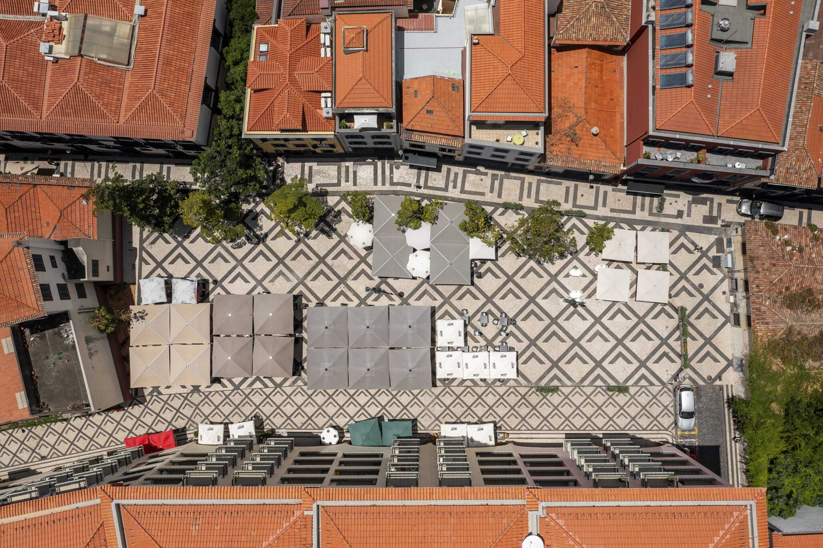 Une vue aérienne d’une cour dont le sol est décoré de motifs, entourée de bâtiments aux toits recouverts de tuiles rouges.