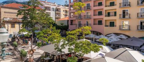 A courtyard with outdoor seating and umbrellas, surrounded by multi-story buildings with balconies.