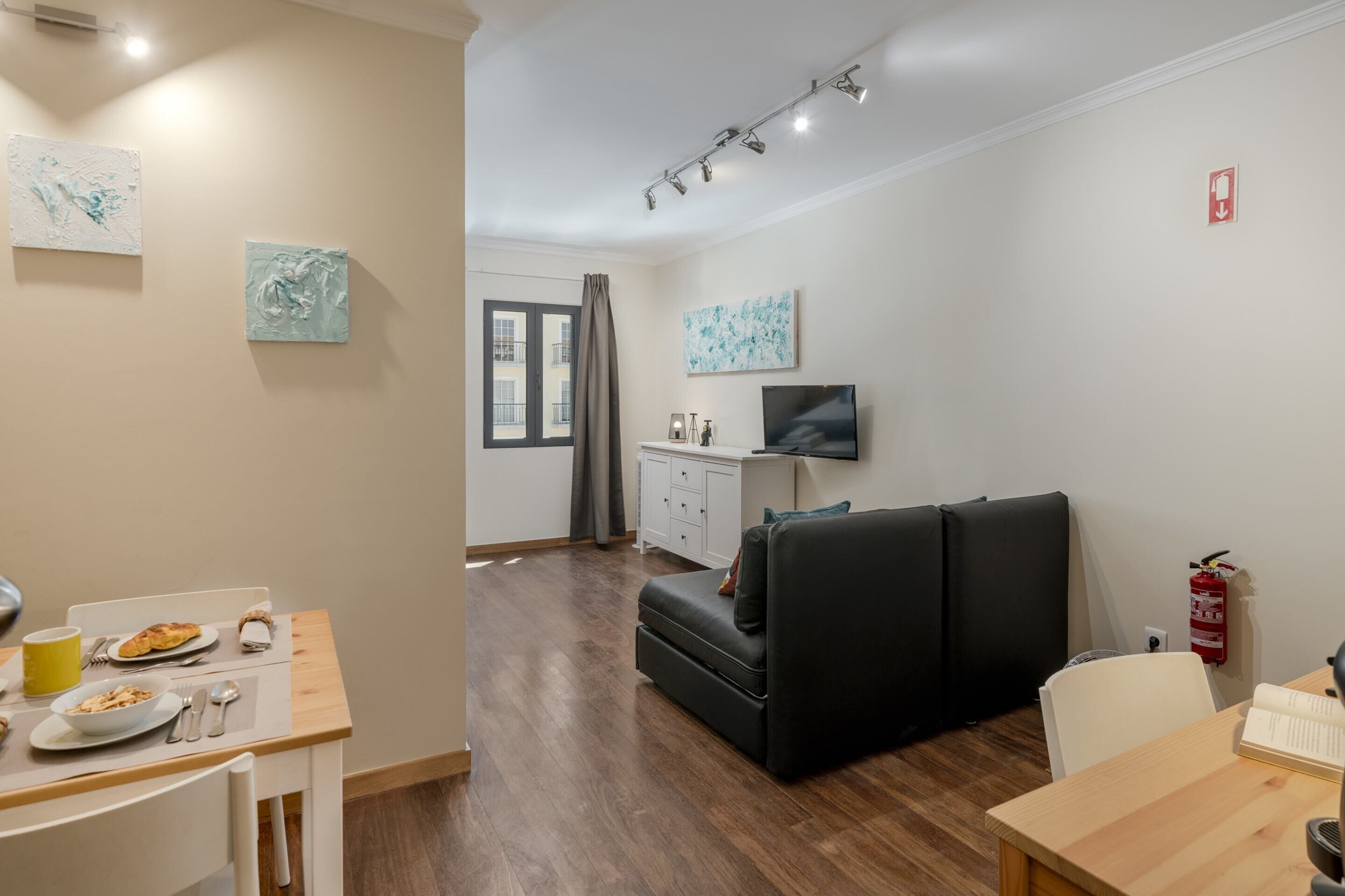 Een moderne woonkamer met een bank, een eettafel met borden en bestek, een televisie en kunstwerken aan de muur.