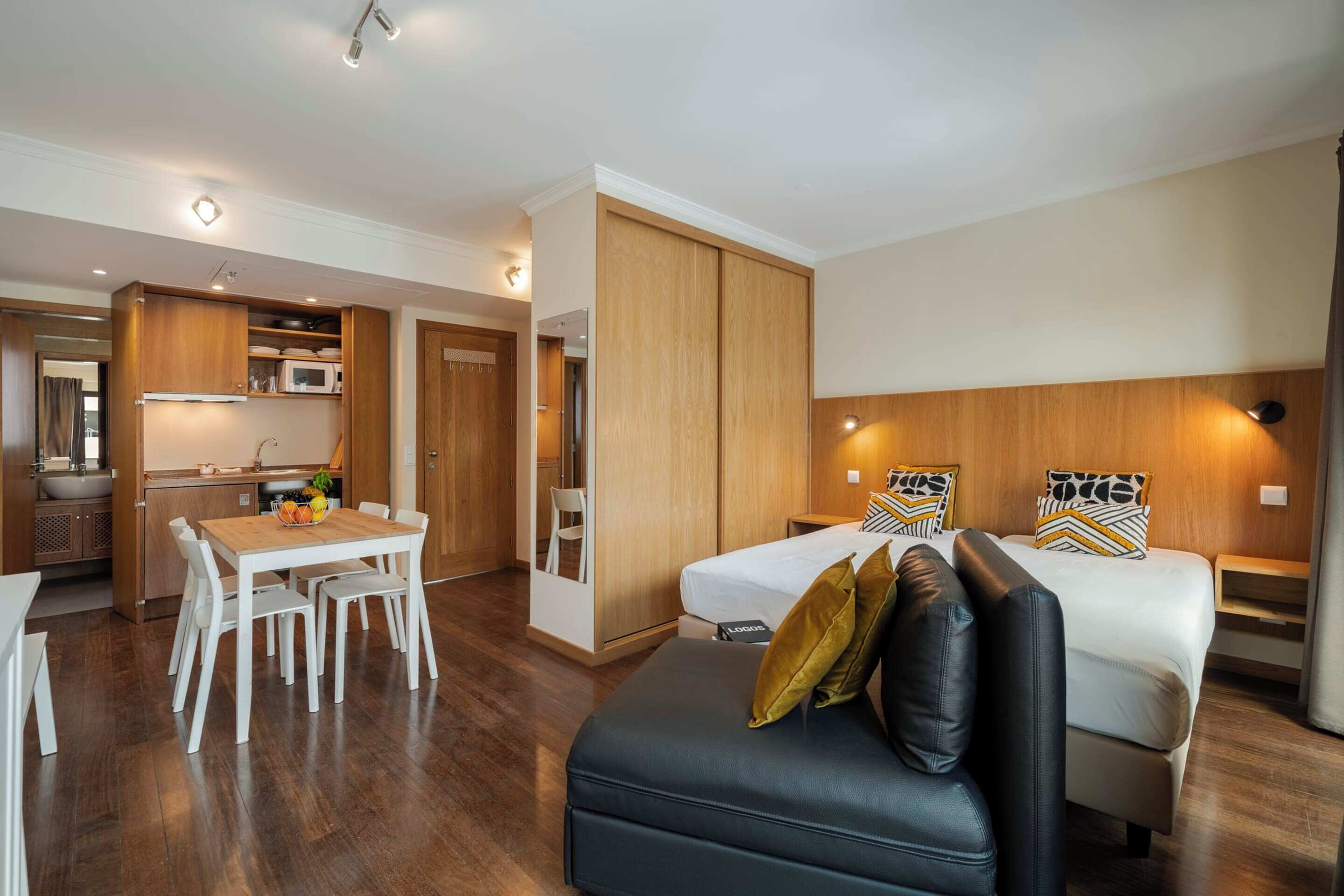 Quarto de hotel moderno com cama, sofá, área de refeições e cozinha compacta.