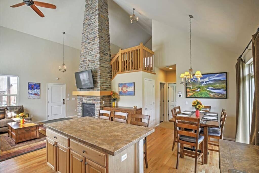 A spacious kitchen with a central island, a stone fireplace, and a dining area with wooden chairs.