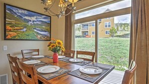 Comedor con una mesa de madera para seis personas, una araña y un cuadro grande de paisaje.