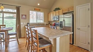 Una cocina con armarios de madera, un refrigerador de acero inoxidable, un microondas y una isla grande con taburetes de bar.