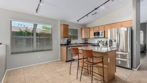 A modern kitchen with wooden cabinets, stainless steel appliances, and a large island with bar stools. - Serenity Haven with Private Pool in Gilbert (Gilbert)