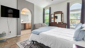 A bedroom with a bed, a ceiling fan, a TV mounted on the wall, a dresser, and a window with curtains. - Serenity Haven with Private Pool in Gilbert (Gilbert)