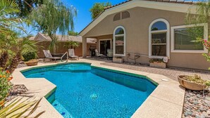 A swimming pool with a patio area, a covered seating area, and a house with a tiled roof and arched windows. - Serenity Haven with Private Pool in Gilbert (Gilbert)