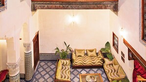 A traditional interior with a tiled floor, a sofa set, a wooden bench, and a hanging light fixture. - Dar Drissi (Fes)