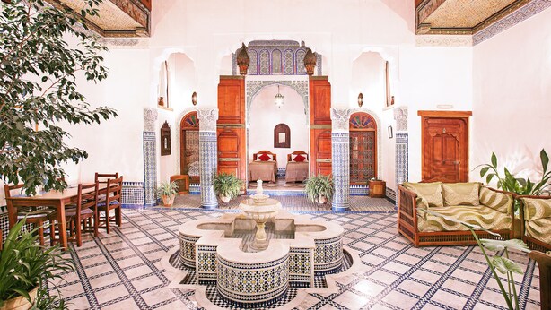 A courtyard with a fountain, seating area, and a bed in the background. - Dar Drissi (Fes)