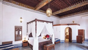 A four-poster bed with a canopy, a wooden nightstand, a small table, and a checkered floor. - Dar Drissi (Fes)