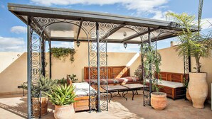 A covered patio area with a wooden bench, a table, and potted plants. - Dar Drissi (Fes)