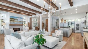 A spacious living room with a fireplace, white sofas, and a large window overlooking a scenic landscape. - WaterColor Presidents Row w/ LSV/golf cart, 6 Bikes, Private Pool! Steps to Beach Club, Sleeps 18! (Santa Rosa Beach)