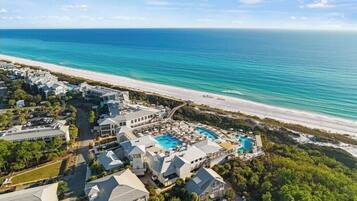 A resort with multiple buildings, a large swimming pool, and a beach view.