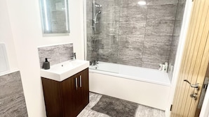 A modern bathroom with a glass-enclosed shower, a white bathtub, and a wooden vanity. - Captivating 2-bed Apartment in Bedford (Bedford)