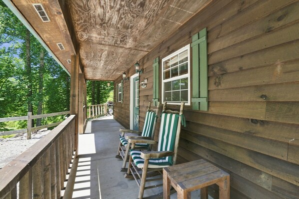 A wooden porch with a covered area, wooden railings, and a row of striped chairs.