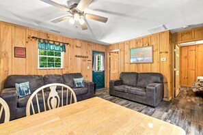 Ein Interieur einer Hütte mit zwei Ledersofas, einem Holztisch und einem Deckenventilator.