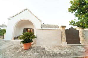 A building with a white facade, an arched entrance, a potted plant, and a gated entrance.