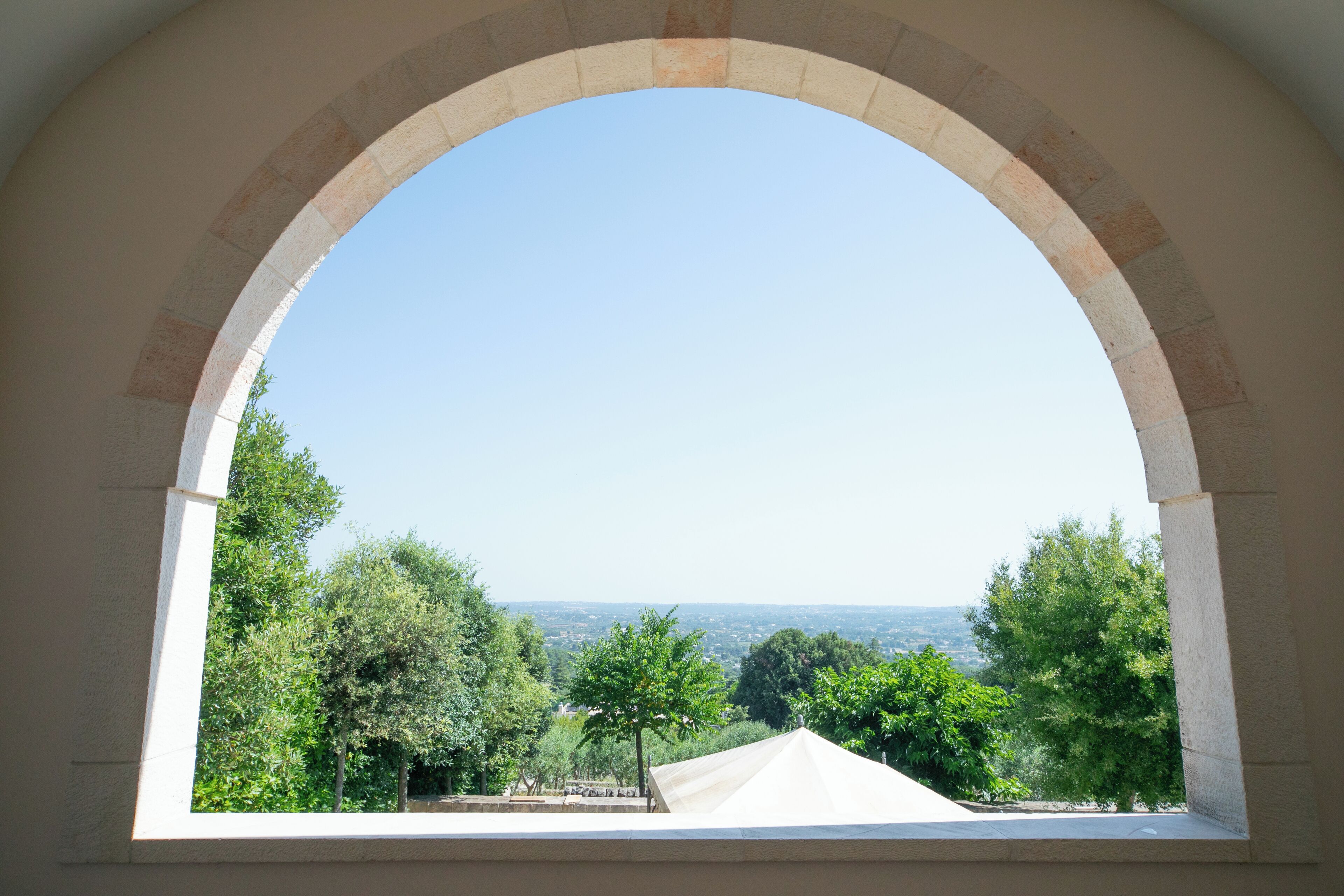 Vista attraverso una finestra ad arco su un paesaggio con alberi e un orizzonte lontano.