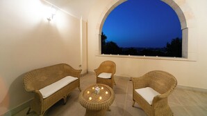 Un balcon agrémenté de meubles en osier, une petite table avec des bougies et une vue sur la ville au crépuscule.