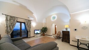 Un salon comprenant un canapé, un téléviseur, une plante, un fauteuil à bascule et un élément décoratif mural.