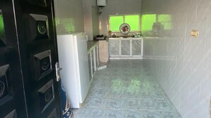 A narrow hallway with a tiled floor, a black door with a window, and a kitchen area with a window and a green screen.