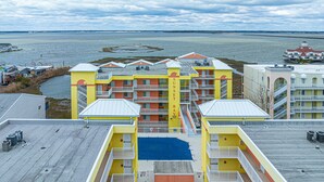 Un hotel de varios pisos con balcones, una piscina en la azotea de color azul y vistas al agua y un puente al fondo.