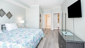 Un dormitorio con una cama, un ventilador de techo, un televisor y una puerta que da a otra habitación.