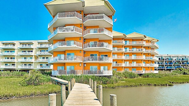Un hotel de varios pisos con balcones, un muelle de madera y una masa de agua al frente.