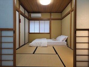 A traditional Japanese room with tatami flooring, a futon bed, sliding shoji doors, and a ceiling fan. - Mizukian (Kyoto)